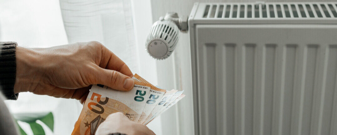 Photo d'une personne près de son radiateur tenant dans ses mains plusieurs billets.